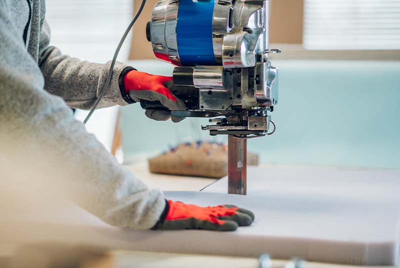 Worker guiding upholstery material through an industrial cutting machine